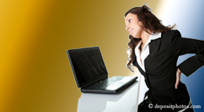 a person Oxford bending over a computer holding her back due to pain